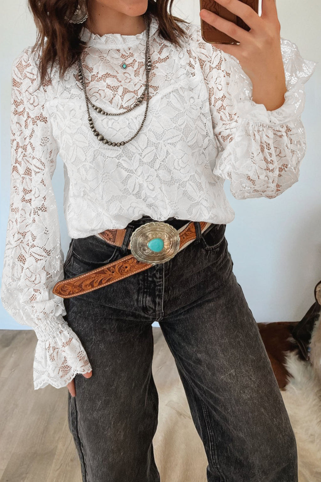 Person wearing a white lace blouse and dark jeans with a belt, standing indoors. Close-up view