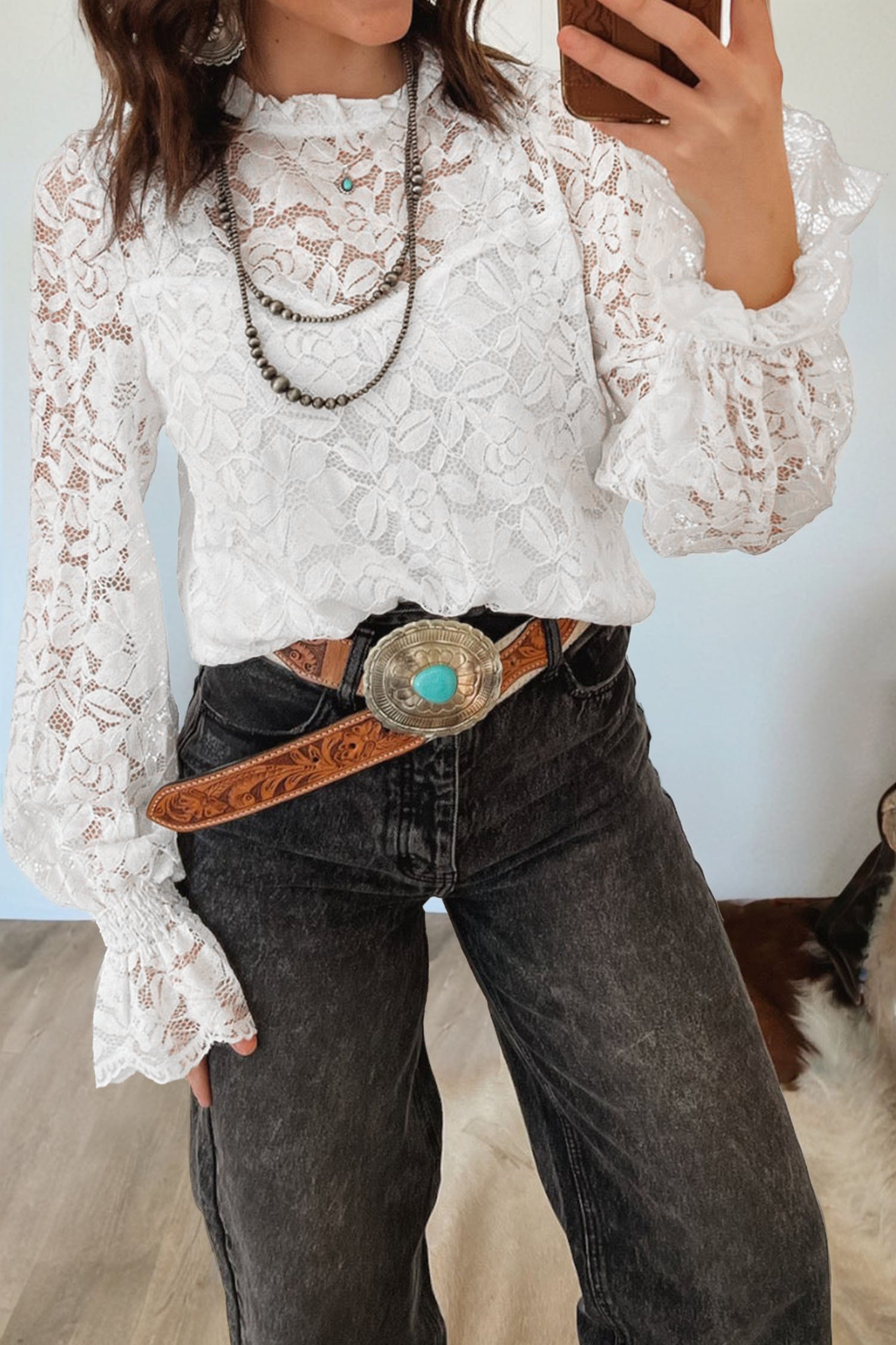 Person wearing a white lace blouse and dark jeans with a belt, standing indoors. Close-up view
