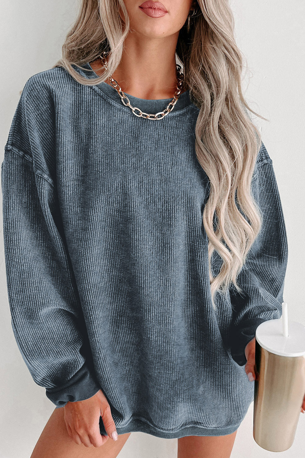 Woman wearing a blue oversized sweater holding a metallic cup against a white background