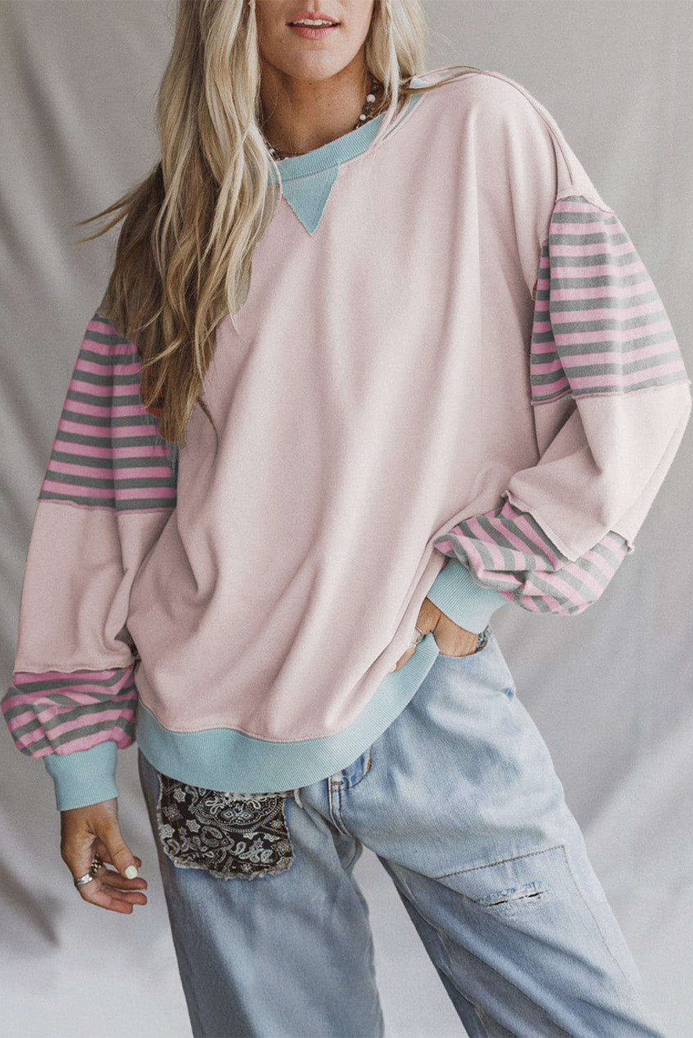 Person wearing a pastel pink and striped long-sleeve top with light blue jeans on a plain background