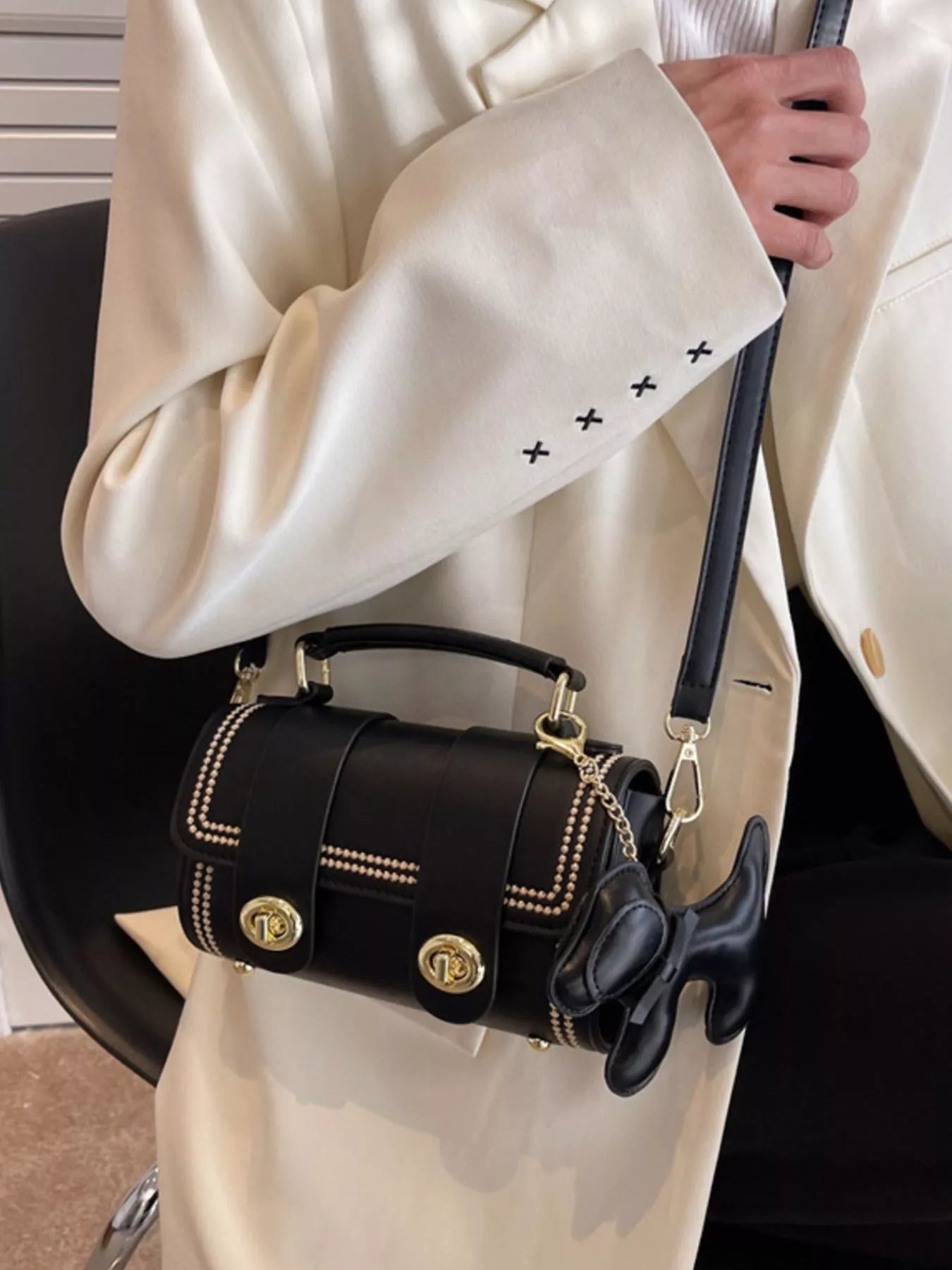 Black handbag with gold accents held by a person wearing a beige coat.
