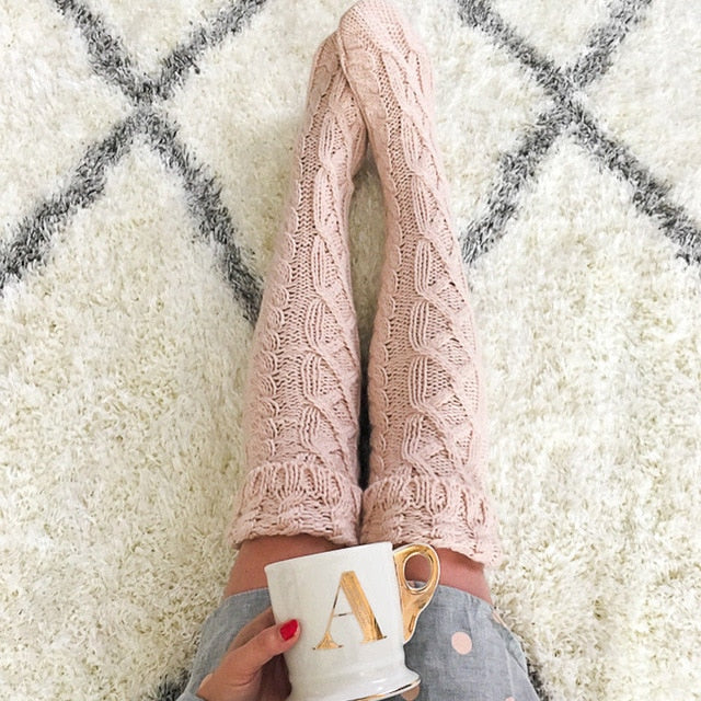 Person wearing pink knitted leggings holding a mug on a fluffy white rug with black geometric patterns.