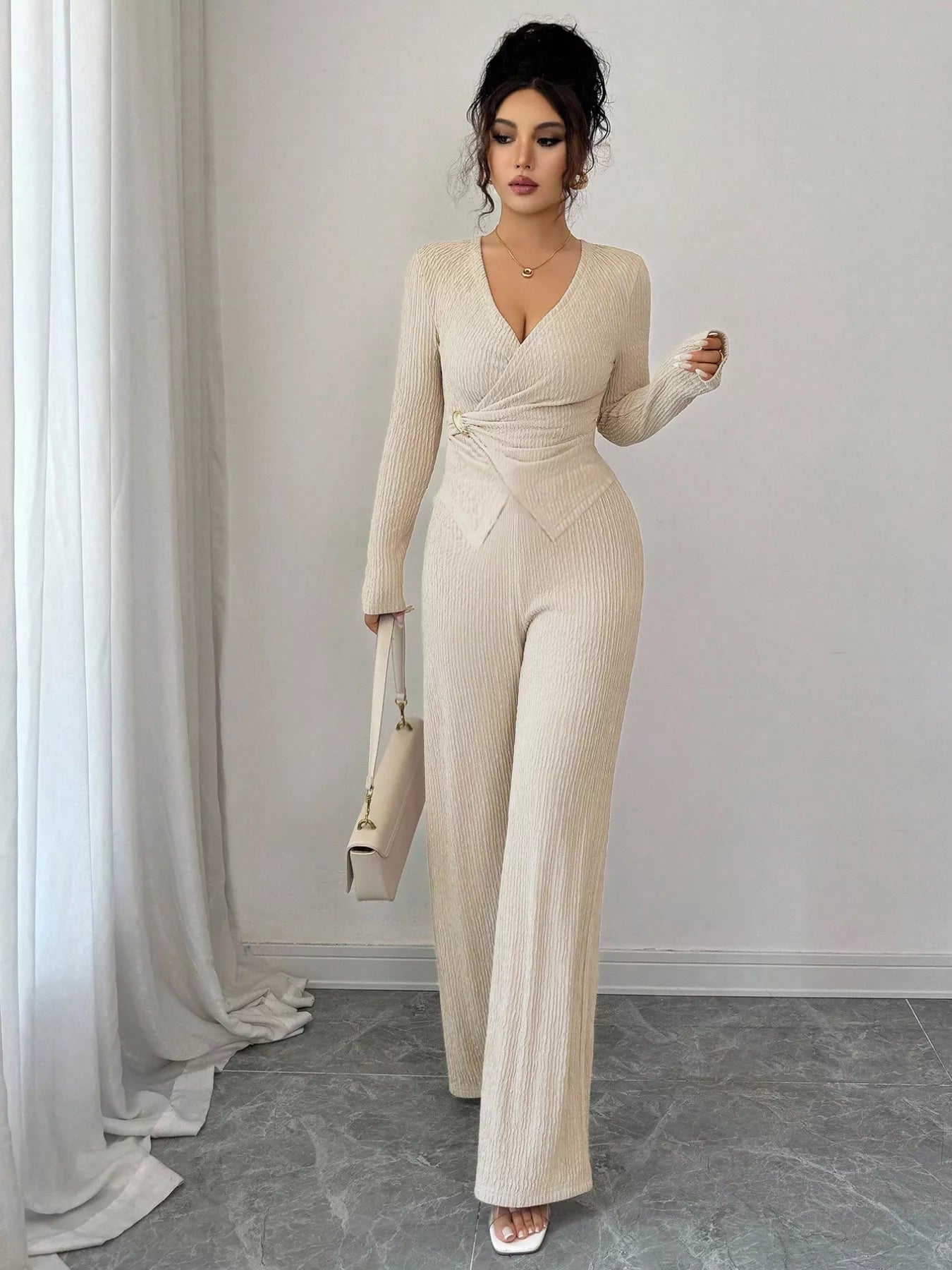 Woman wearing a beige ribbed jumpsuit standing in a room with white curtains.