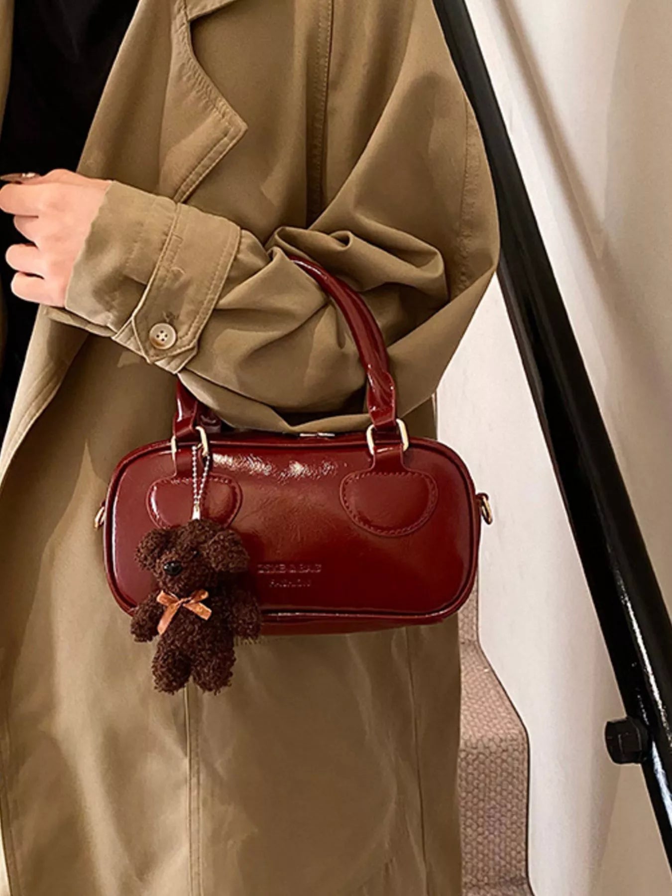 Person holding a red handbag with a decorative charm, wearing a beige coat.