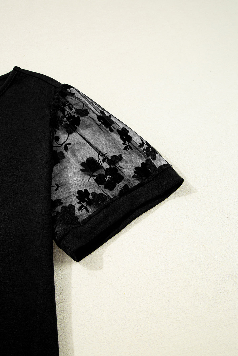 Black floral sheer fabric draped over a black garment on a white background