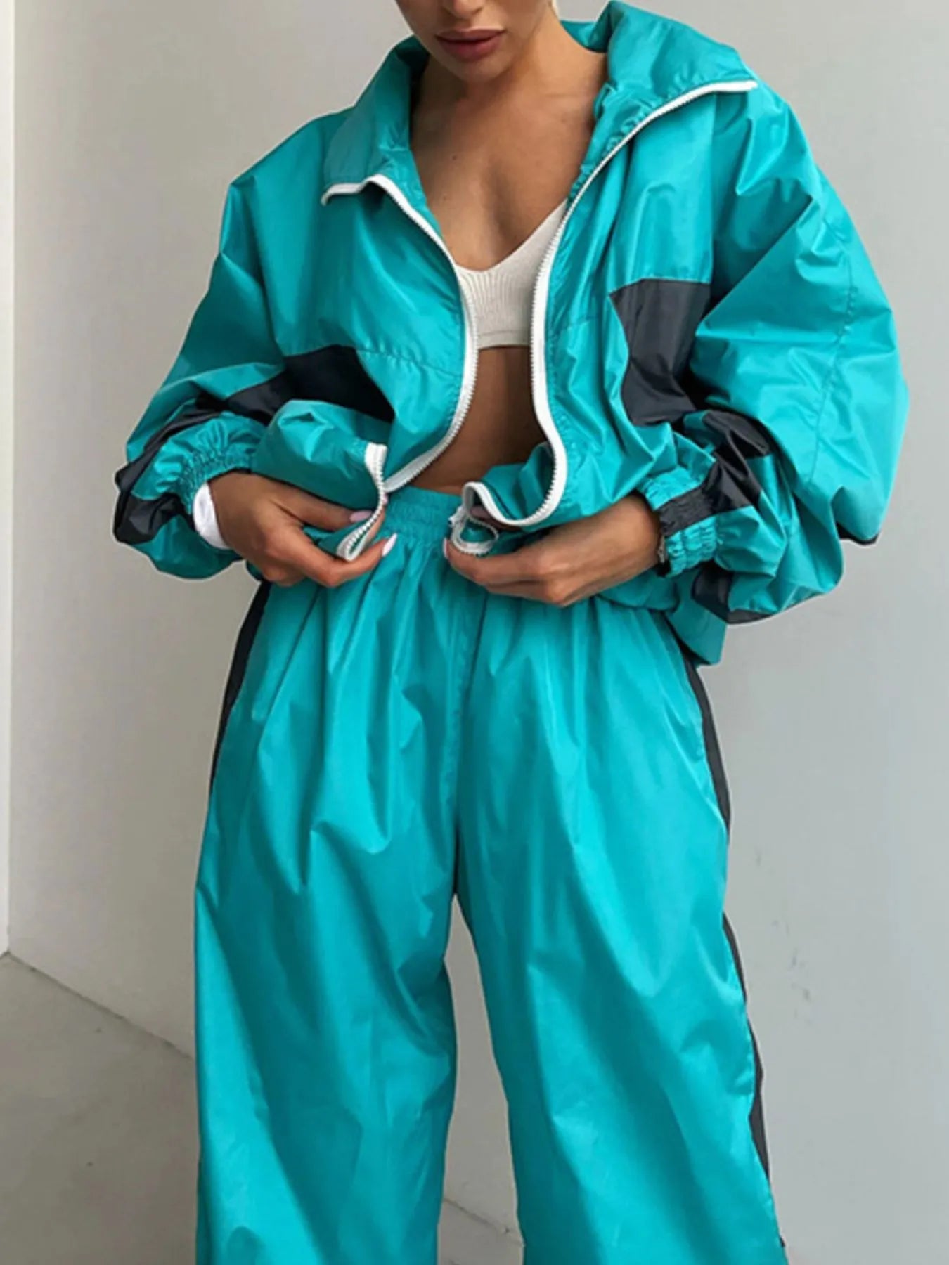 Person wearing a teal tracksuit with black accents against a plain background