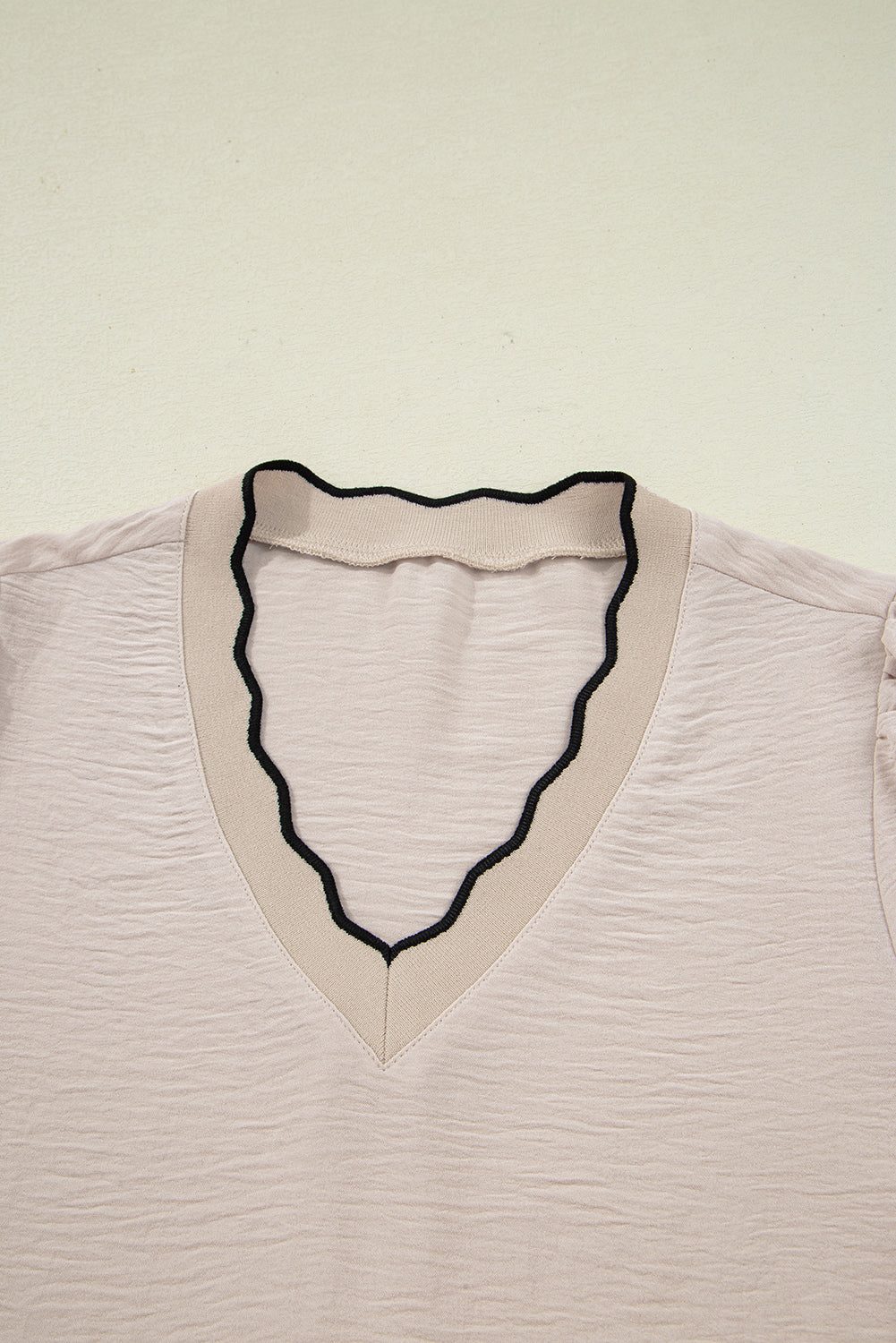 Close-up of a light pink blouse with a black neckline on a beige background