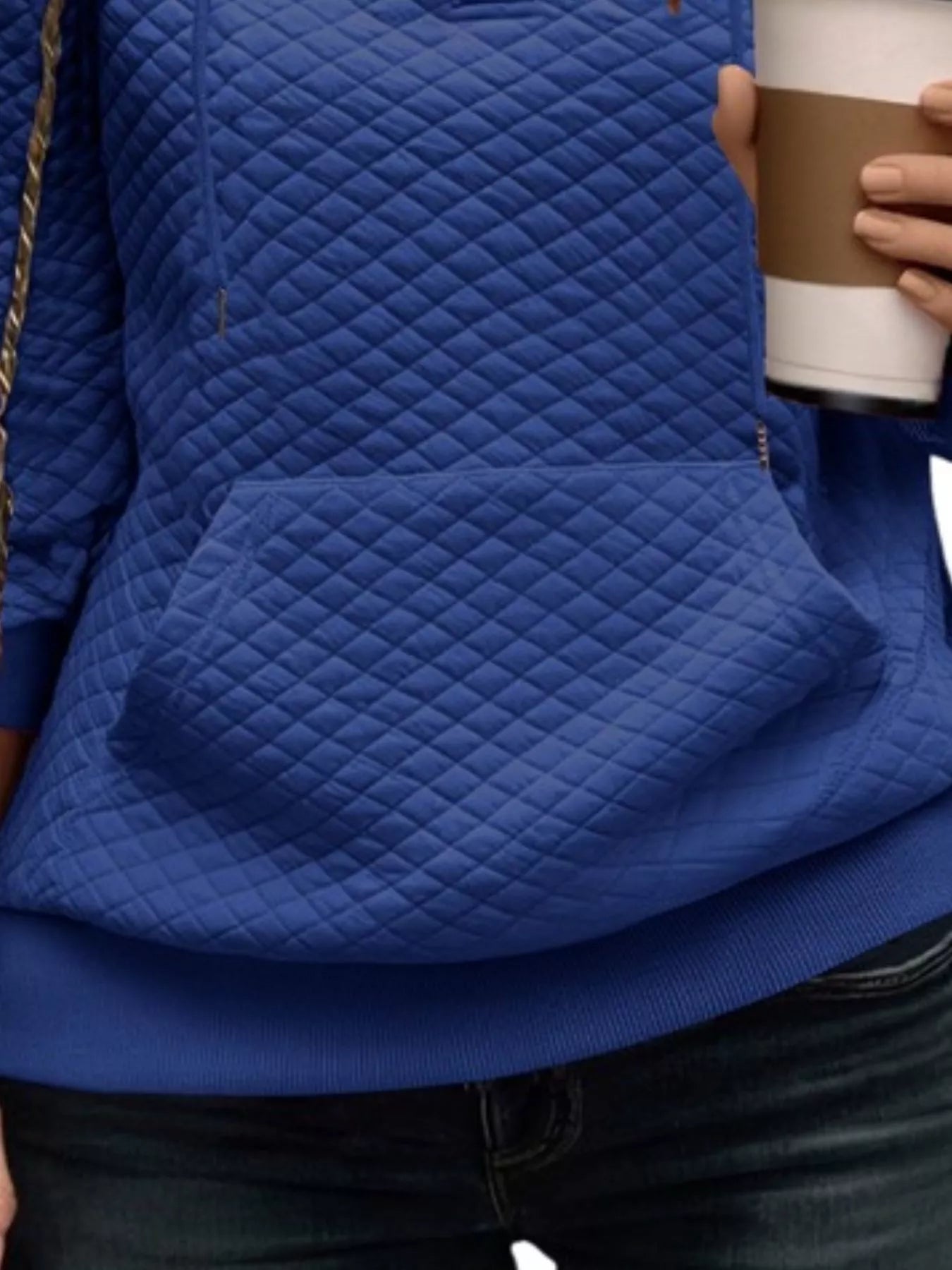 Person wearing a blue quilted jacket holding a coffee cup.