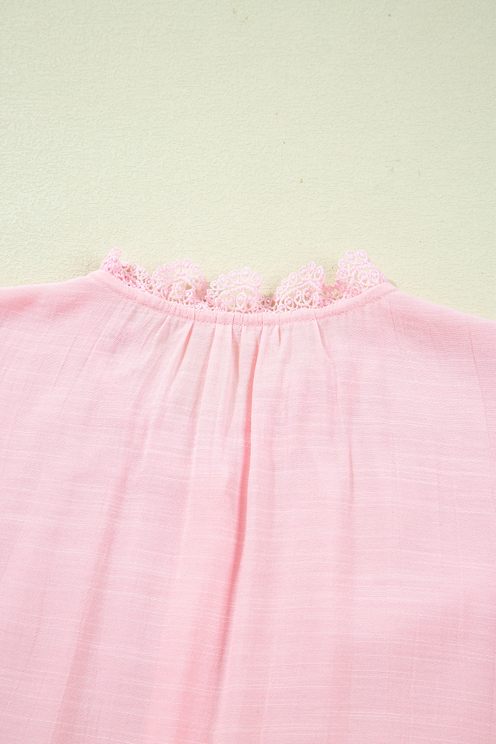 Close-up of a pink garment neckline with lace trim on a light green background