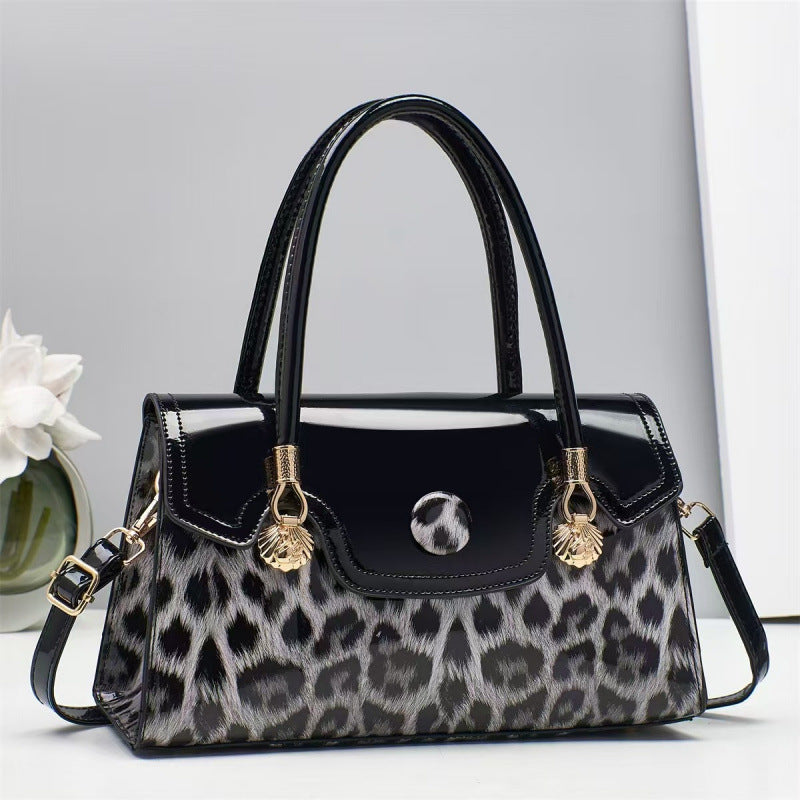 Black handbag with leopard print and gold accents on a light gray background