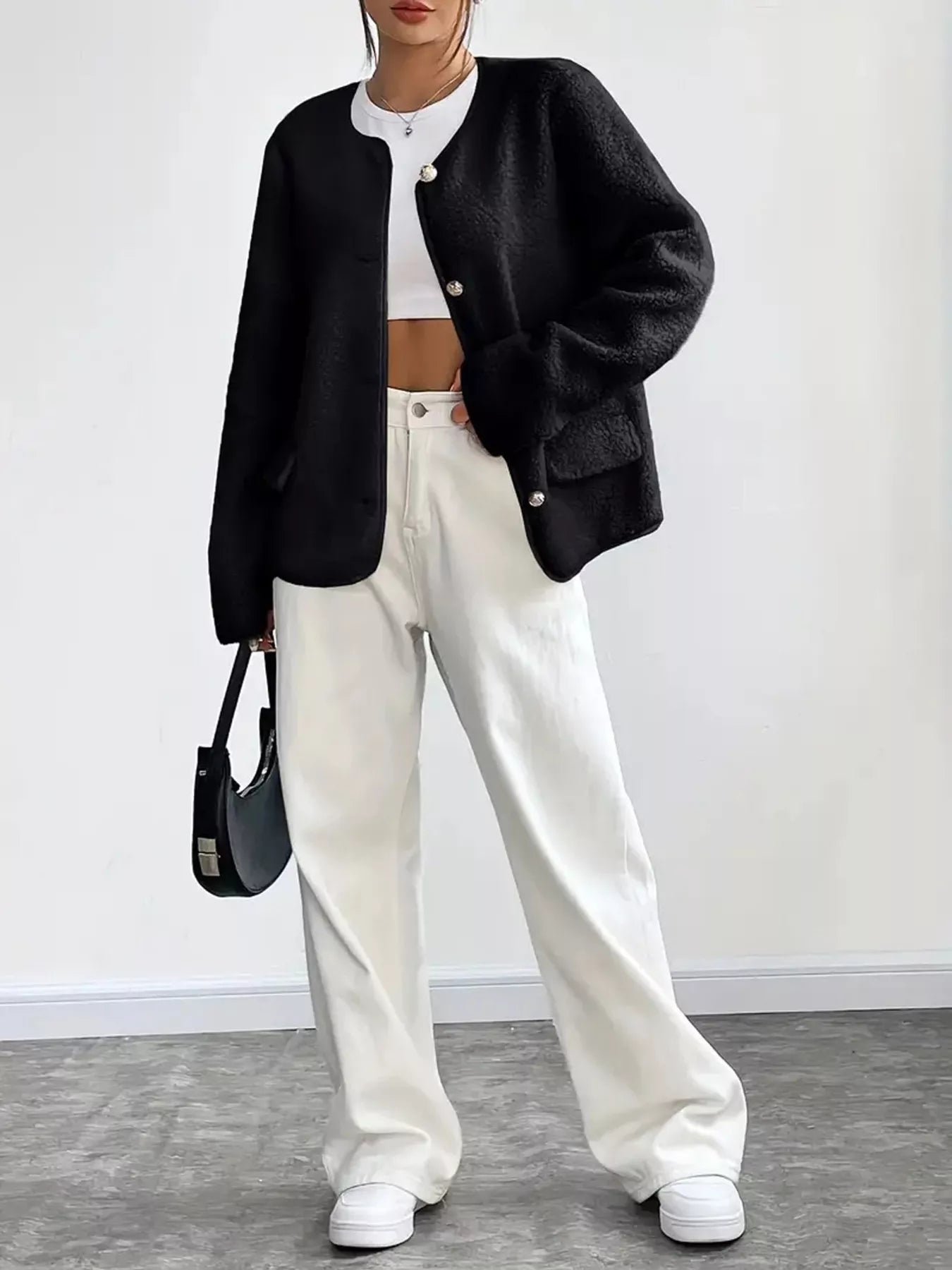 Person wearing a black cardigan, white top, and pants with a black handbag against a white background