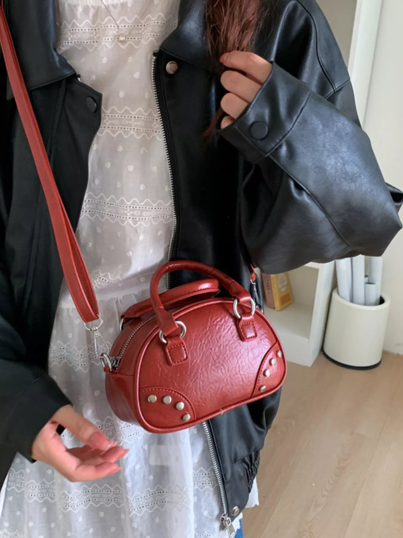 Person holding a red handbag with a white lace dress in the background