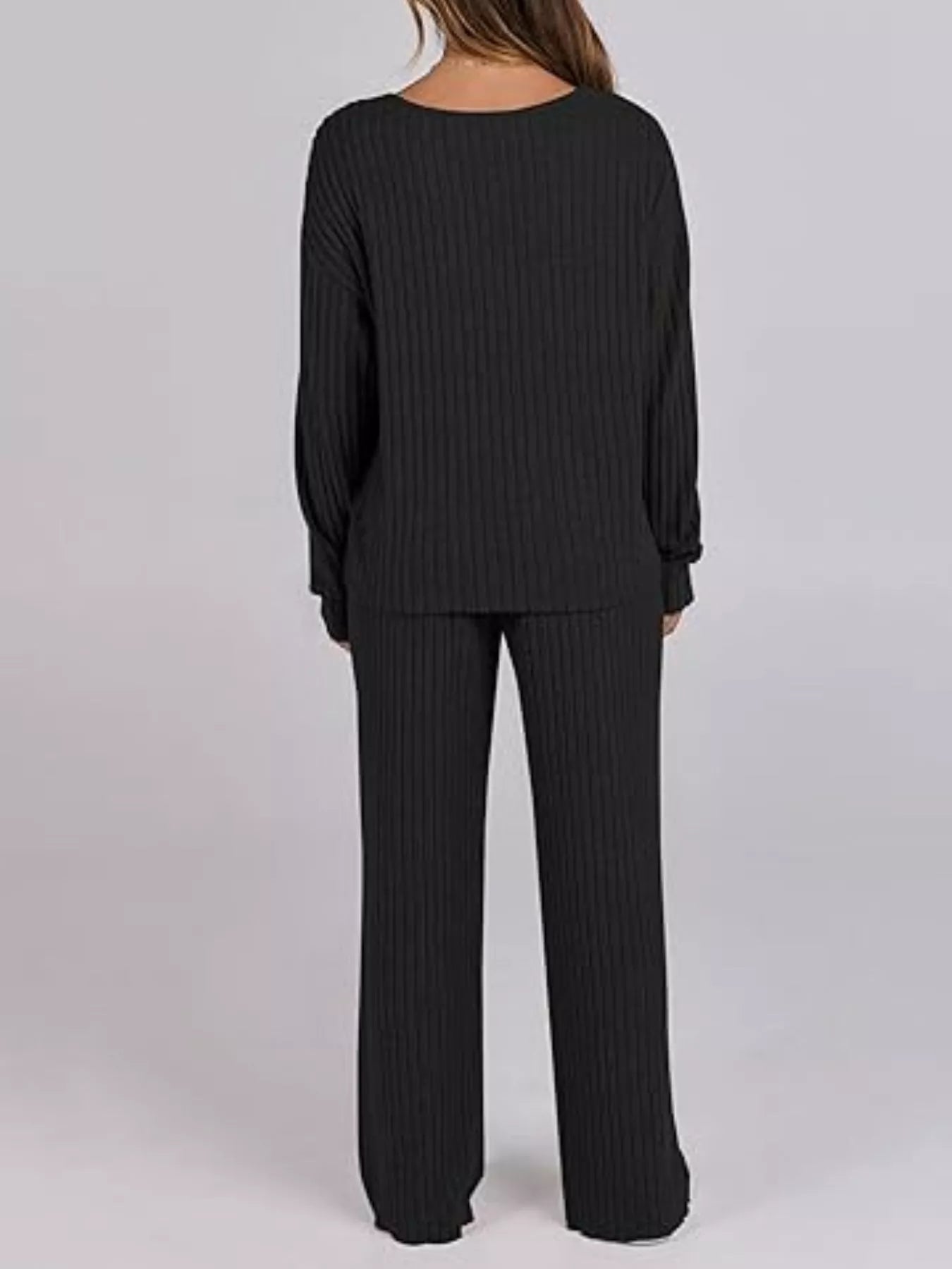 Person wearing a black ribbed sweater and pants on a light gray background