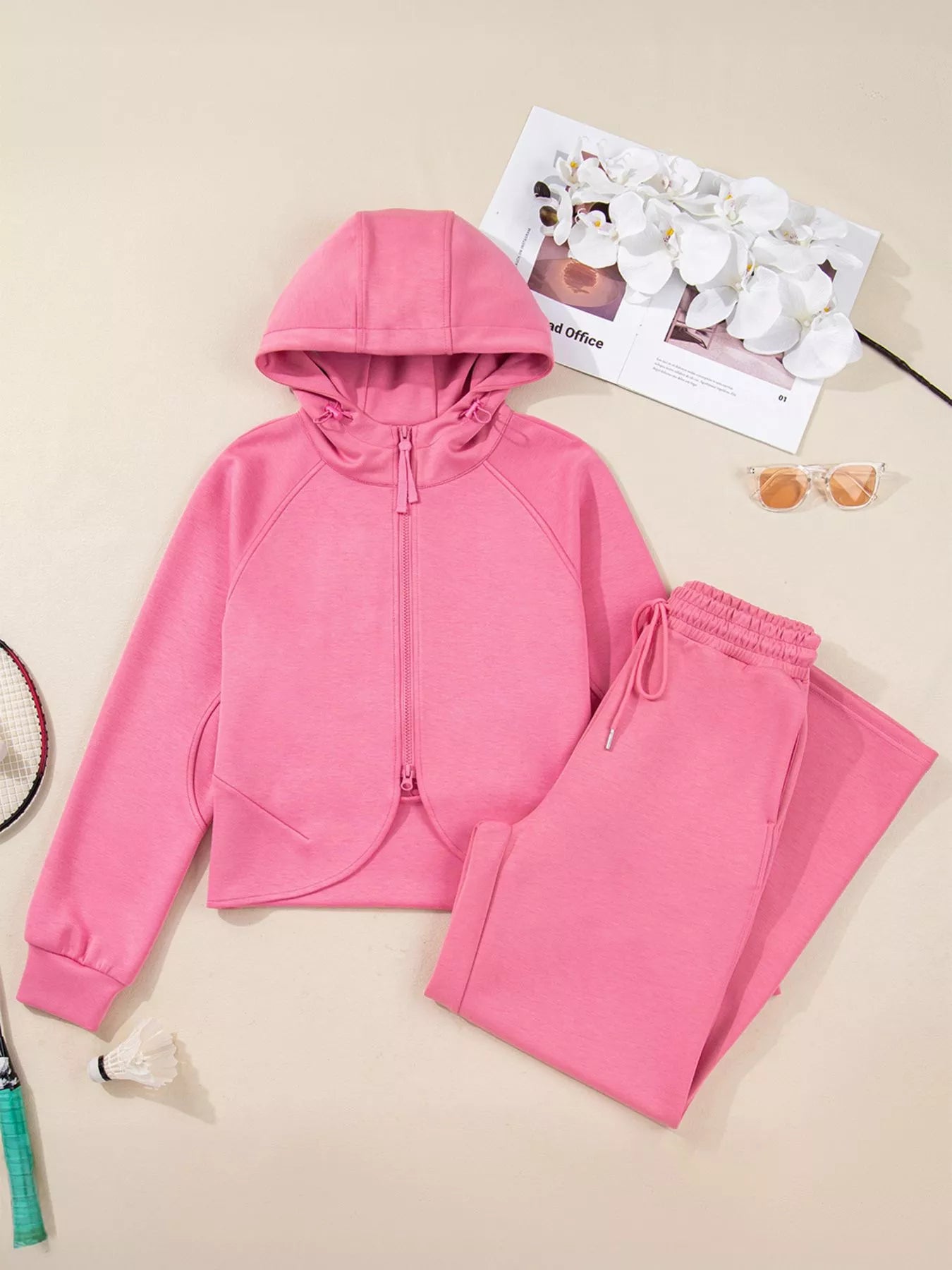 Pink hoodie and pants set on a beige surface with a magazine and earrings.