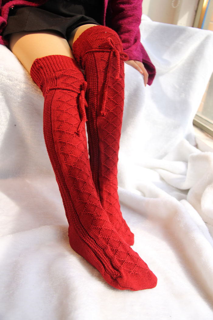 Red knee-high socks with a pattern worn by a person on a white surface.
