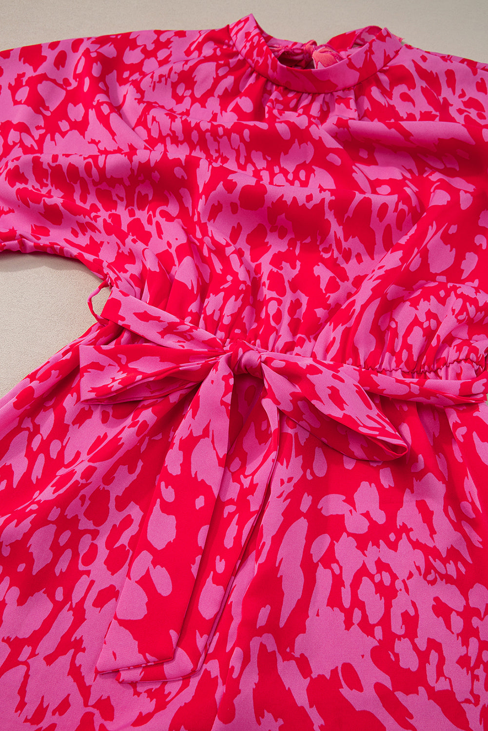Pink and red patterned dress with a tie waist on a neutral background