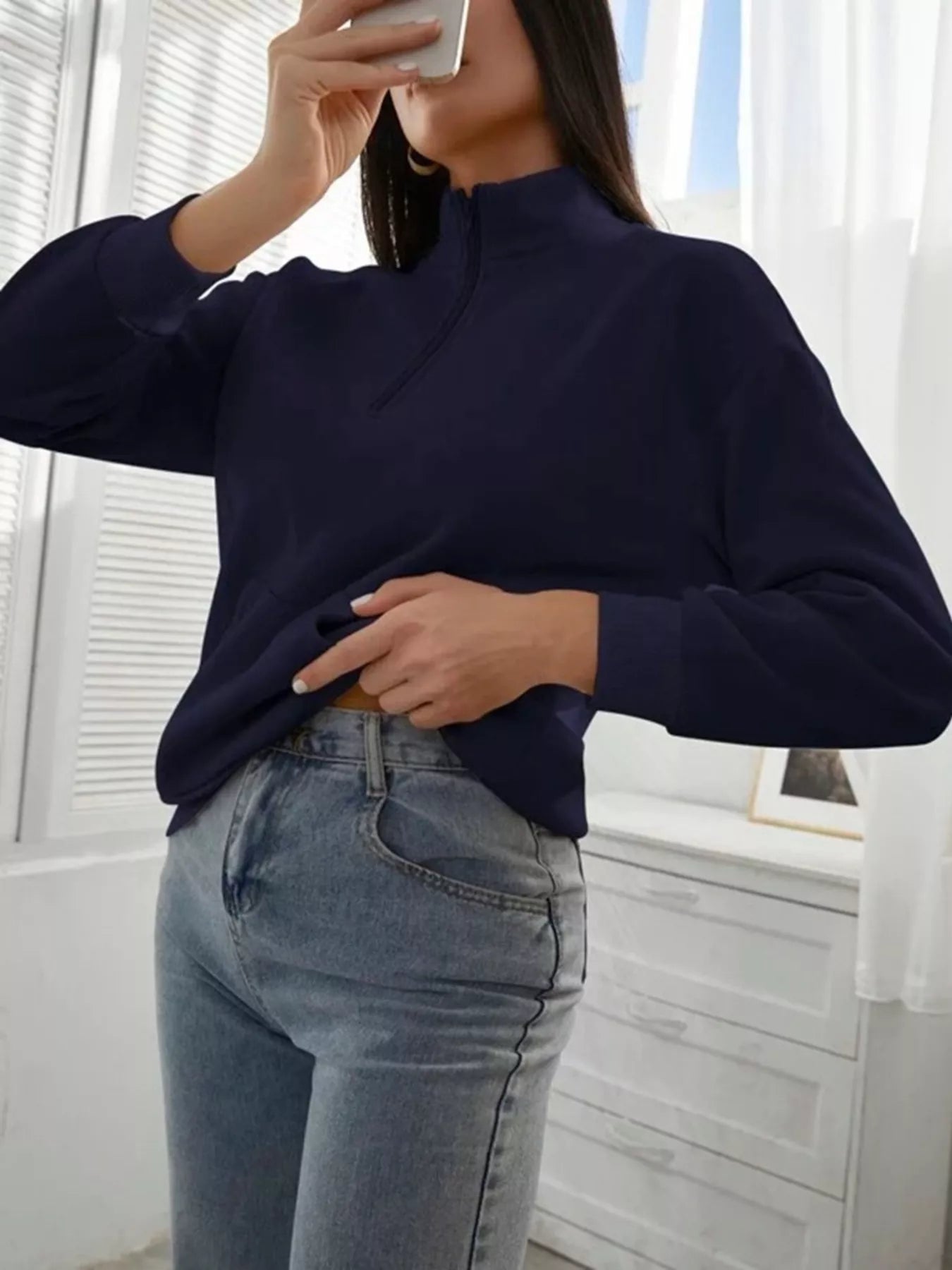 Person wearing a navy sweater and light blue jeans indoors.