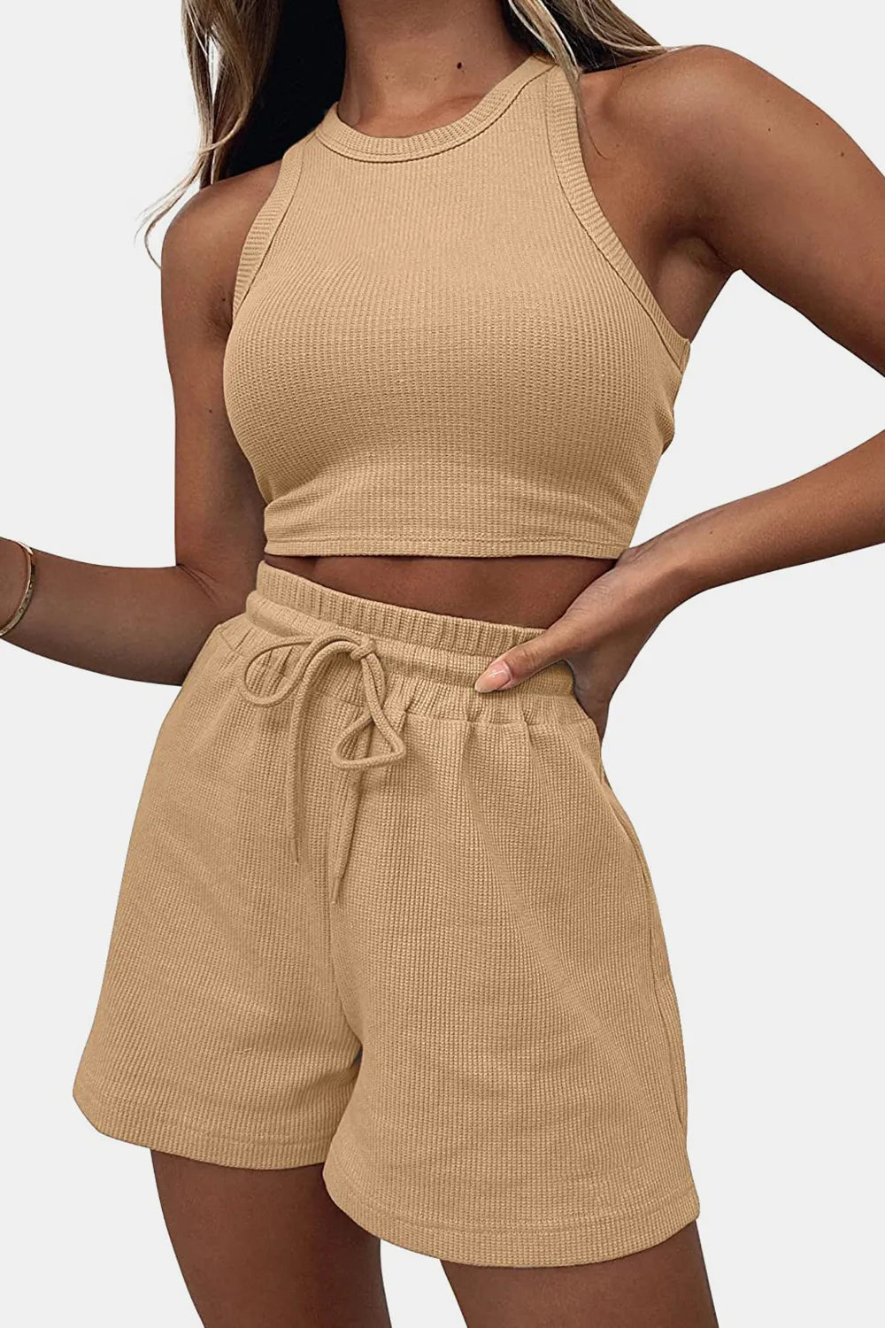 Woman wearing a beige ribbed tank top and shorts set on a plain background
