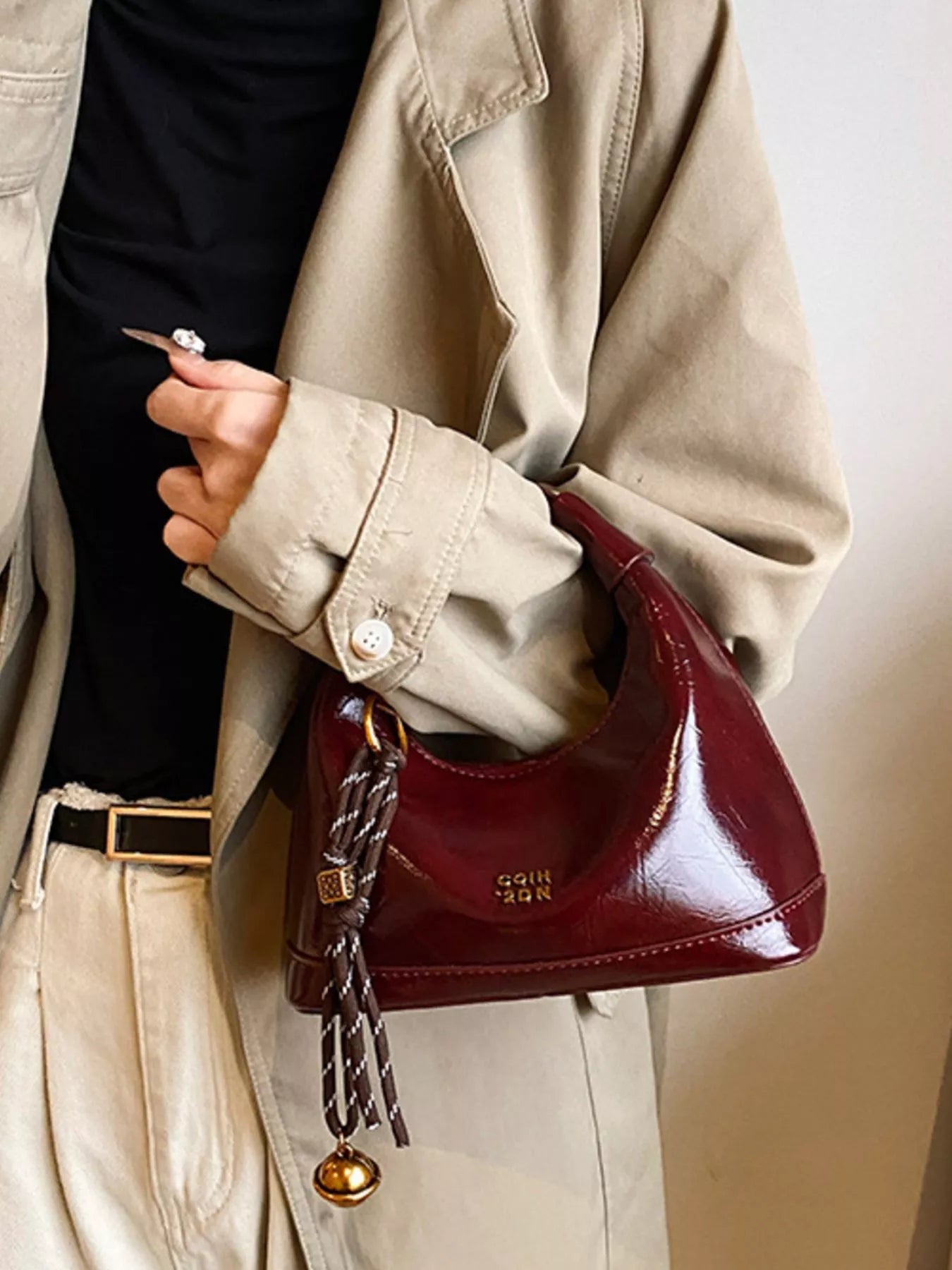 Person holding a burgundy handbag with a gold chain detail, wearing a beige coat.