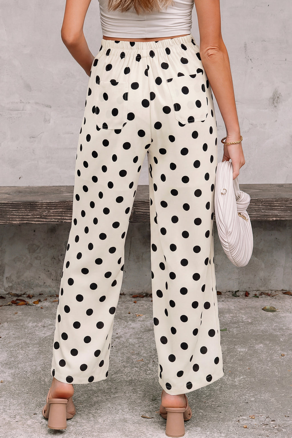 Person wearing polka dot white-black pants standing against a concrete wall. Back view