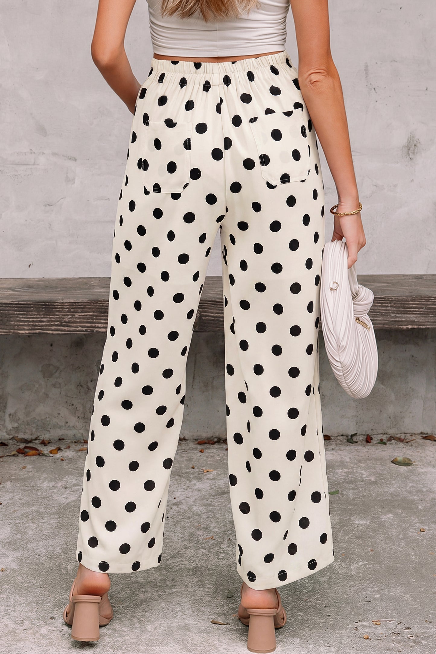 Person wearing polka dot white-black pants standing against a concrete wall. Back view
