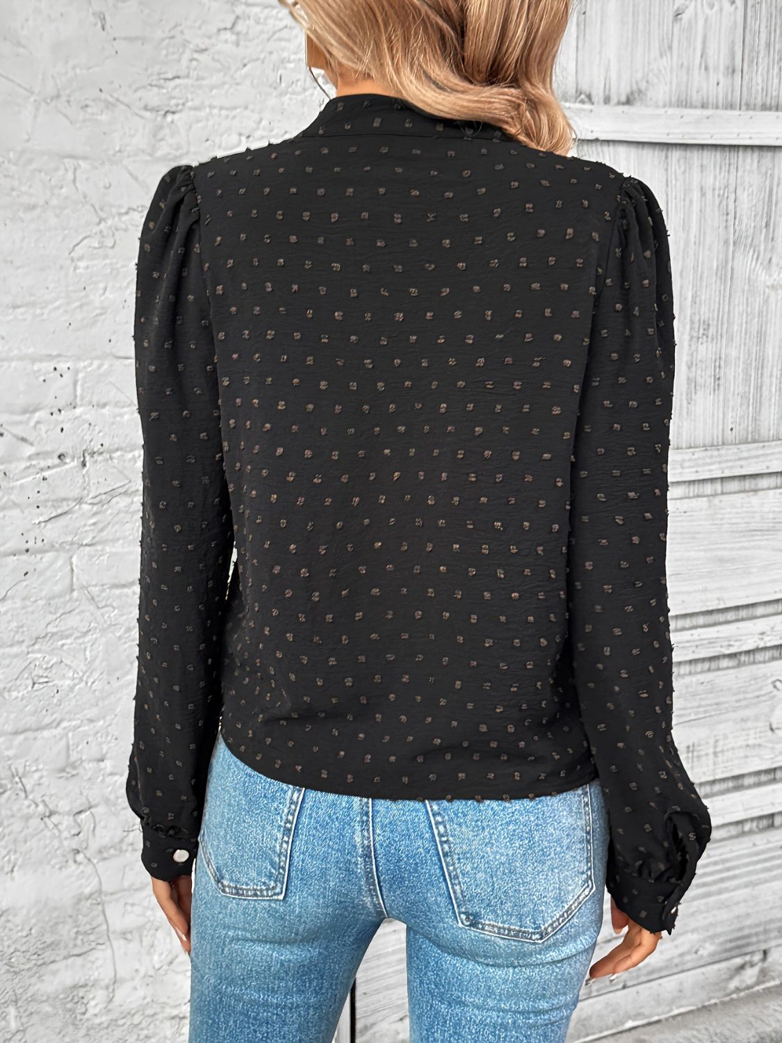 A woman wearing a black long sleeve blouse with a Swiss dot pattern back view
