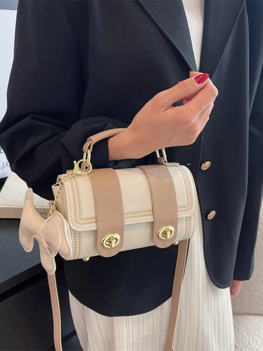 Person holding a beige handbag with gold accents, wearing a black blazer and white dress.