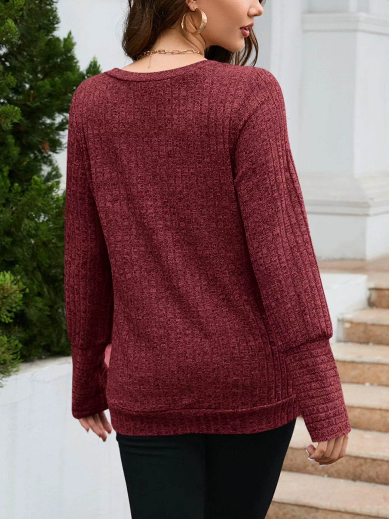 Person wearing a maroon sweater standing on steps with greenery in the background