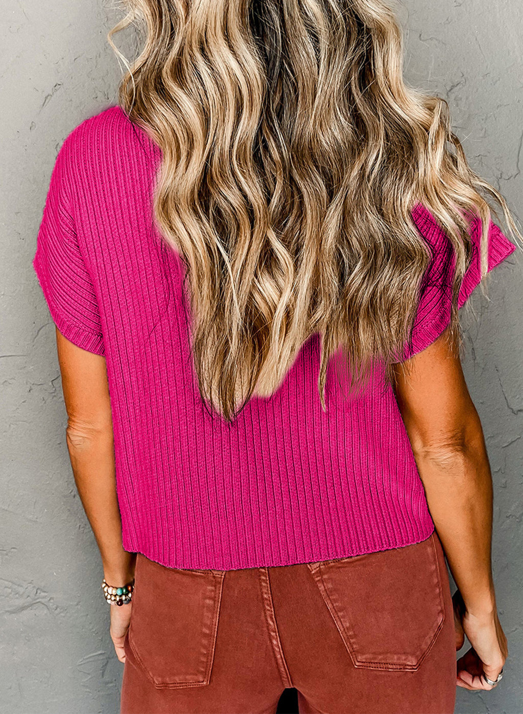 Person wearing a bright pink ribbed top against a gray background