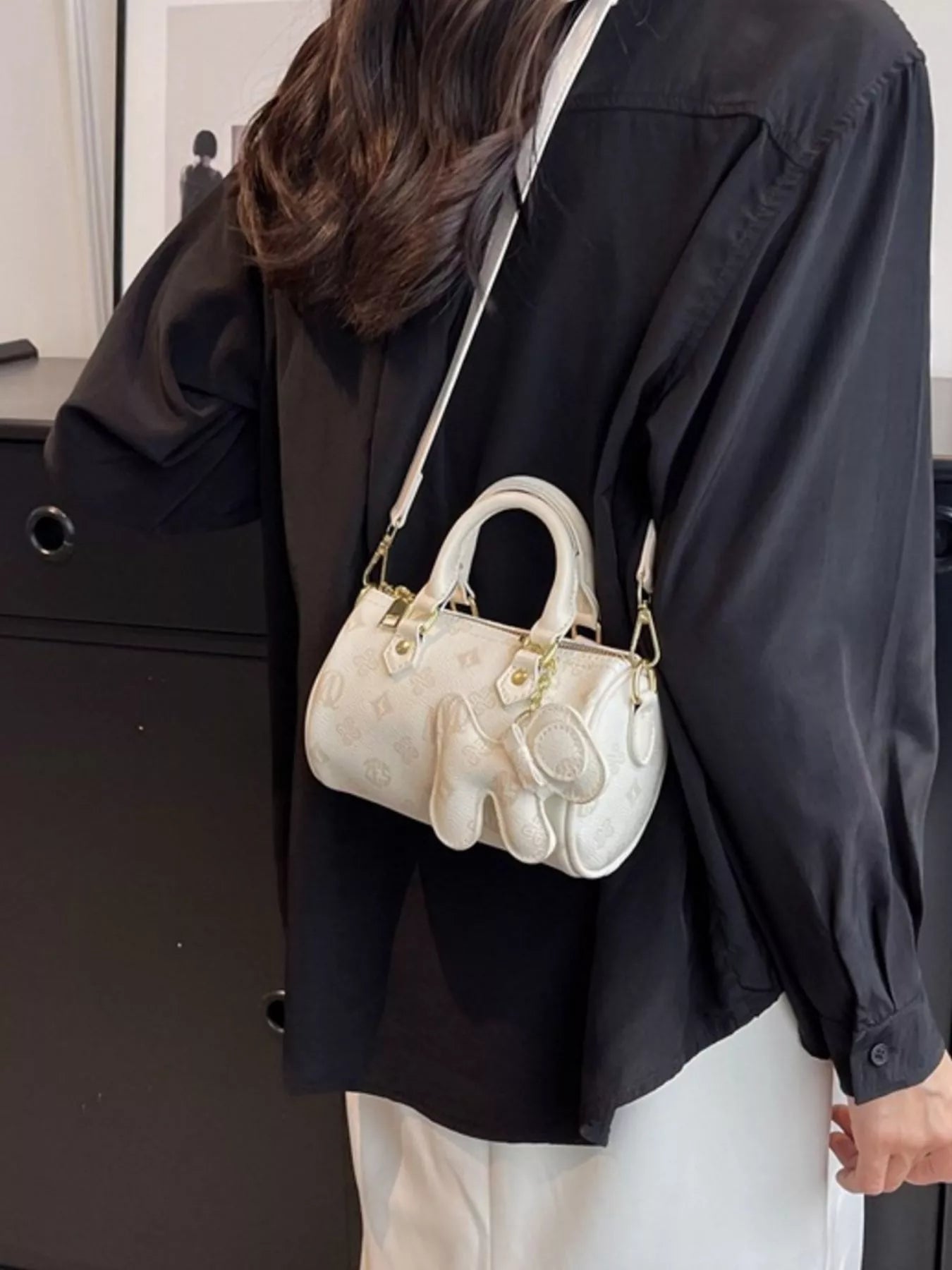 Person wearing a black coat with a white handbag featuring gold accents.