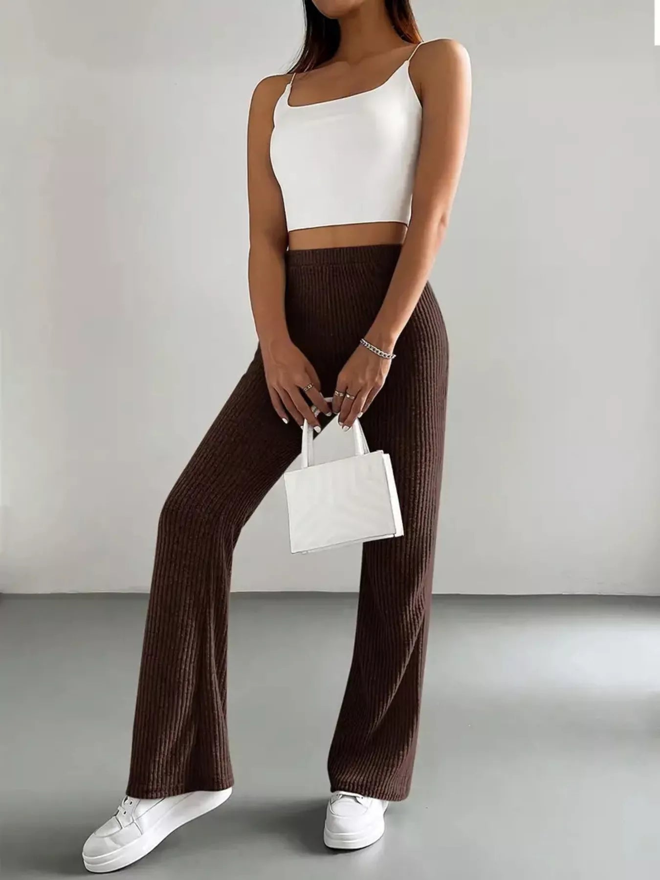 Person wearing a white crop top and brown ribbed pants, holding a small white handbag.