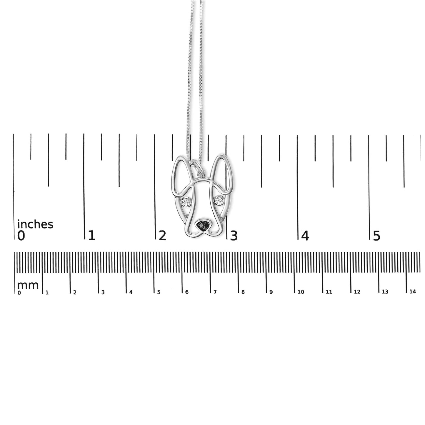 Silver dog pendant with heart-shaped eyes on a chain, measured against a ruler.