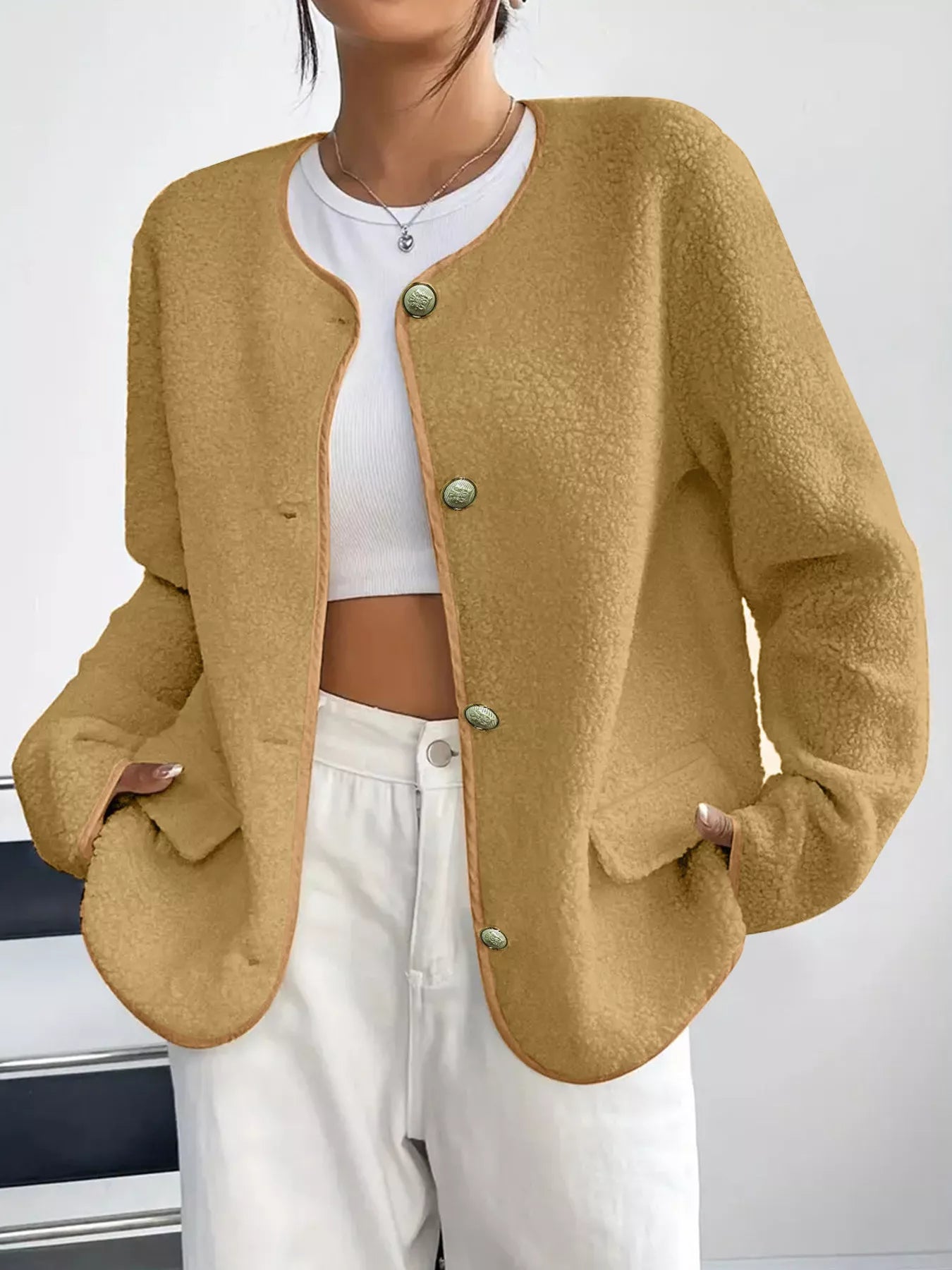 Person wearing a mustard yellow cardigan over a white top and pants on a plain background