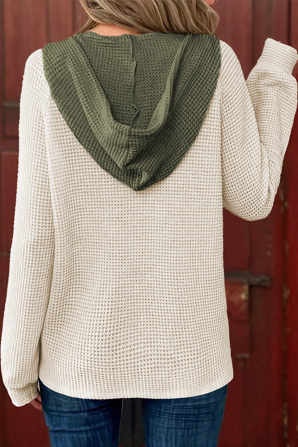 Person wearing a beige knit sweater with a green hood against a red background