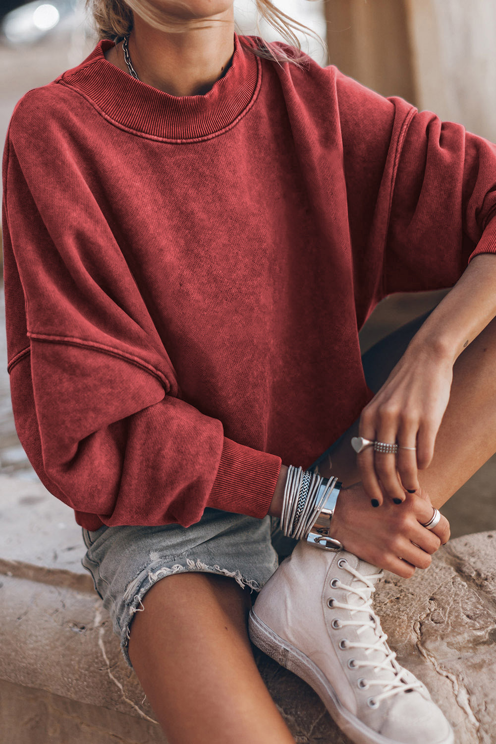 Person wearing a red sweatshirt and white sneakers sitting on a stone surface.