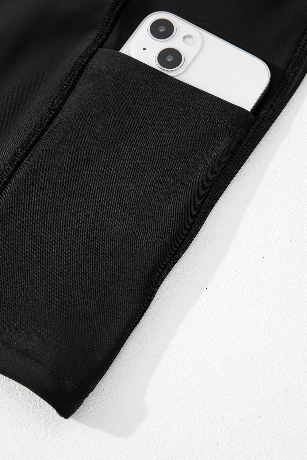 Black jacket with a pocket containing a white smartphone on a white background