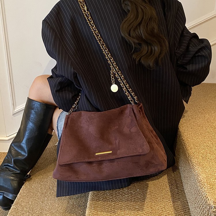 Person wearing a dark pinstripe outfit with a brown suede handbag and black leather boots.