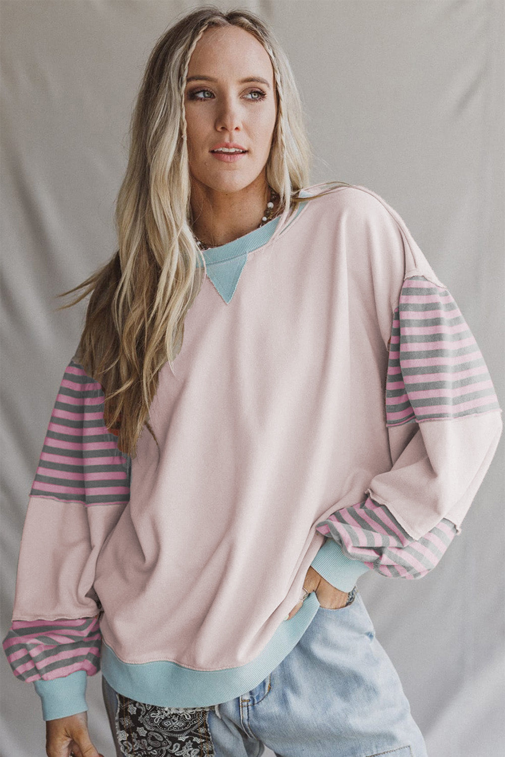 Woman wearing a light pink sweater with striped sleeves against a plain background