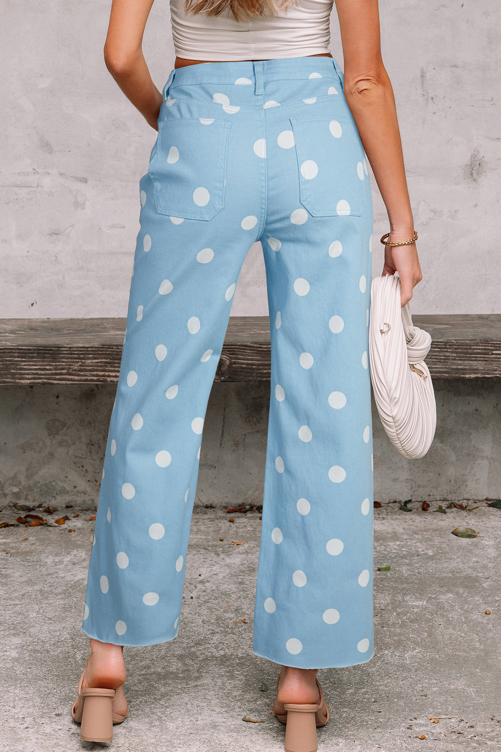 Light blue pants with white polka dots worn by a person, standing against a concrete wall. Back view