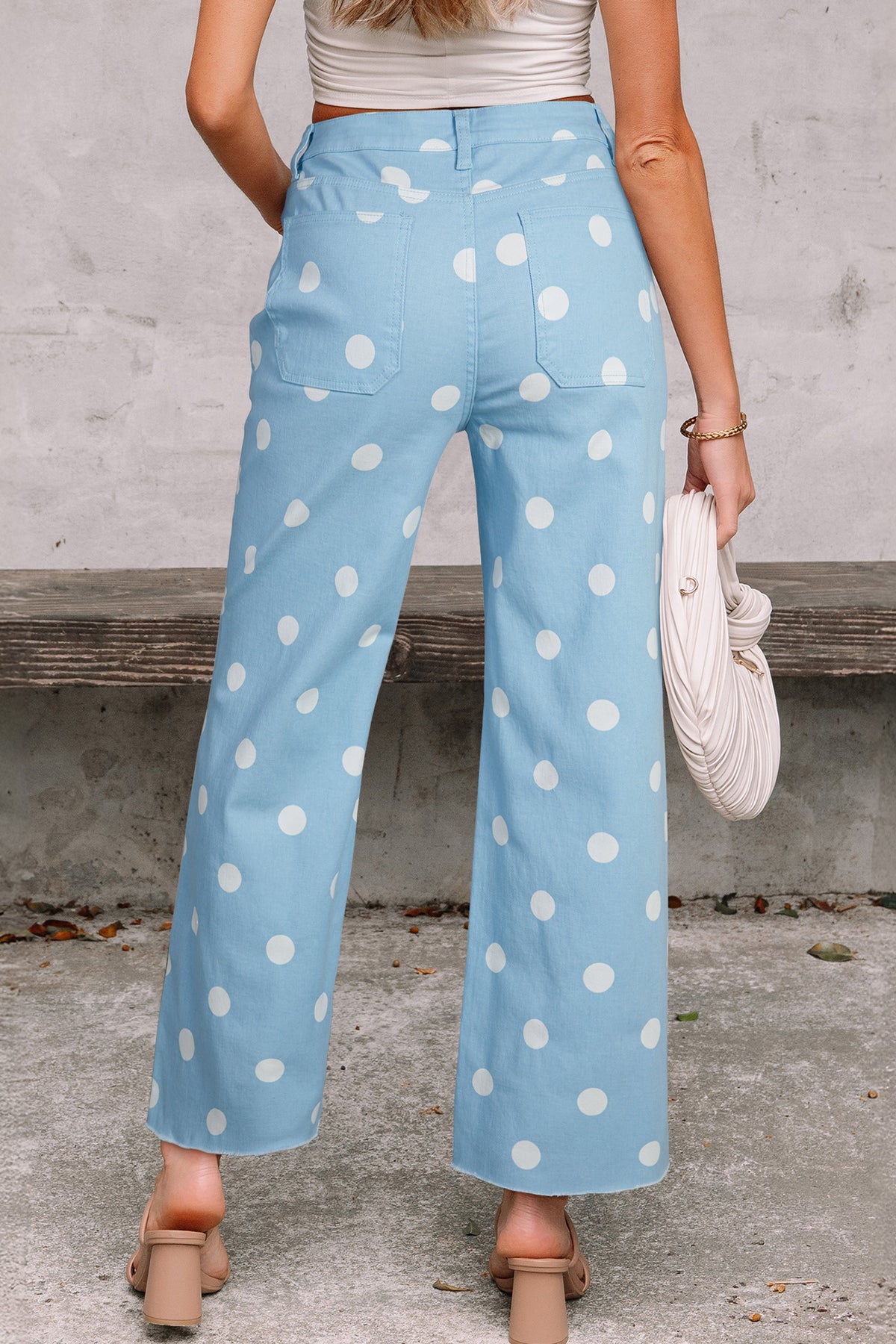 Light blue pants with white polka dots worn by a person, standing against a concrete wall. Back view