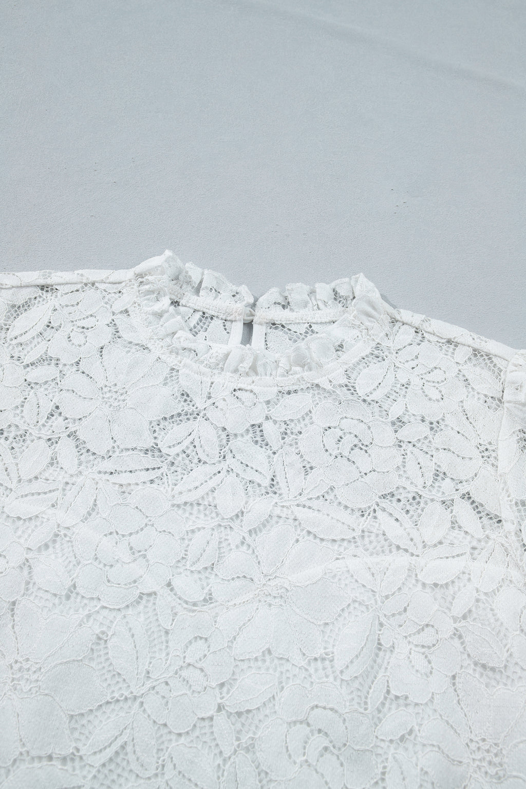 White lace top on a light gray background detailed view