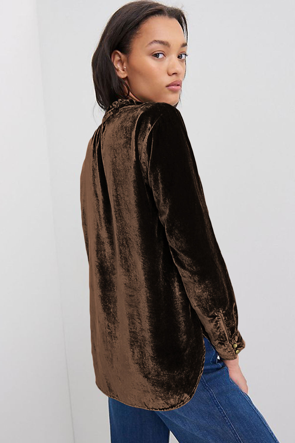 Woman wearing a brown velvet shirt and blue jeans against a white background