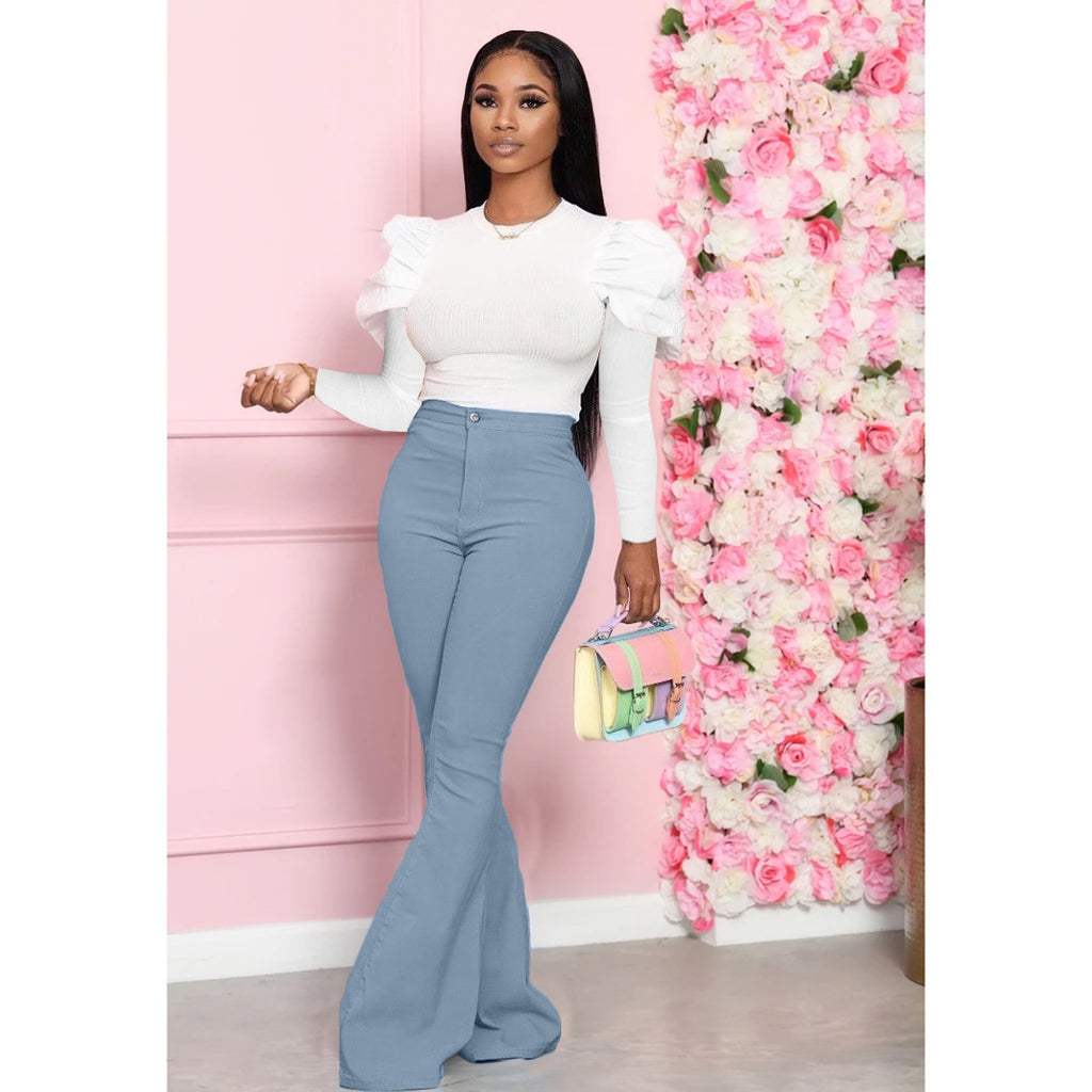 Woman in white top and blue pants standing next to a pink floral wall.