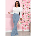 Woman in white top and blue pants standing next to a pink floral wall.
