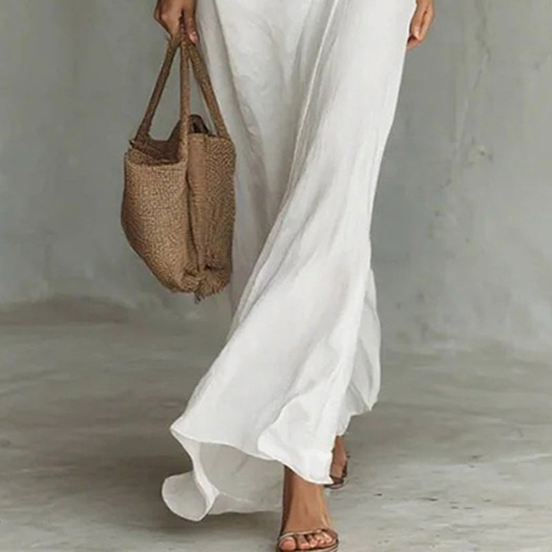 Person wearing a long white dress holding a woven brown bag against a neutral background