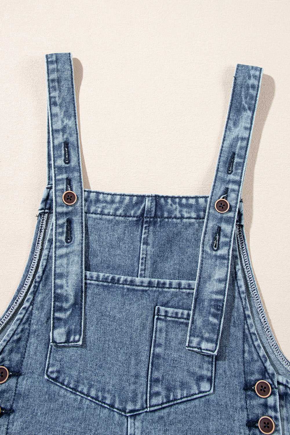 Blue denim overalls with straps on a beige background