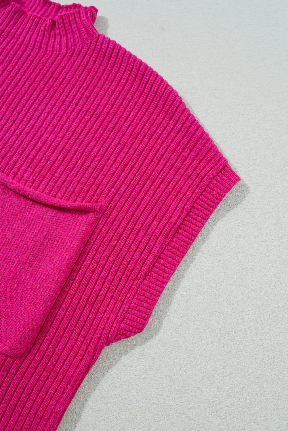 Close-up of a bright pink ribbed sweater on a light gray background