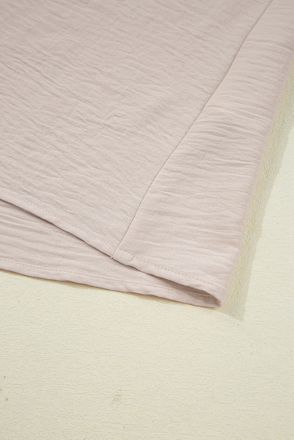 Close-up of a textured fabric with a soft pinkish-purple color on a light beige background.