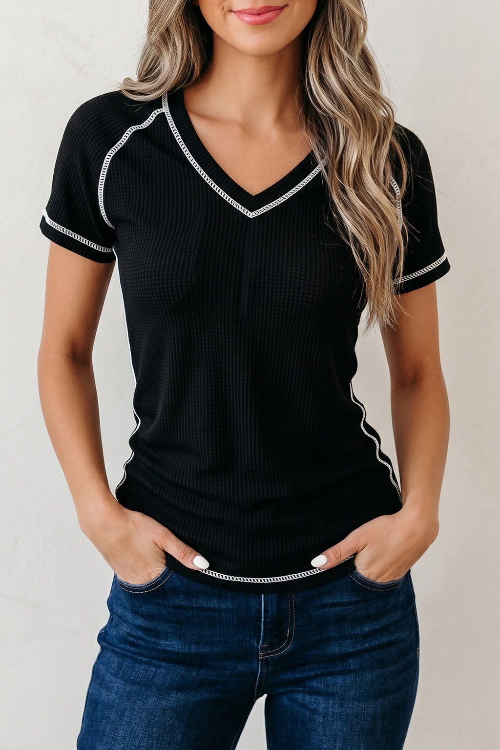 Woman wearing a black ribbed top with white trim and blue jeans against a plain background
