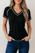 Woman wearing a black ribbed top with white trim and blue jeans against a plain background